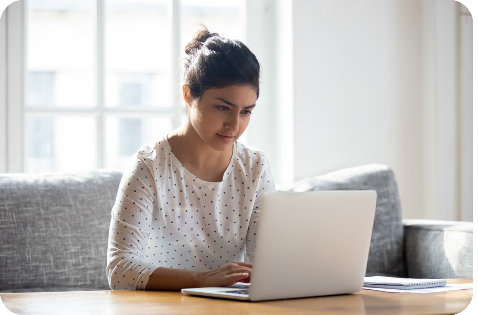 Young woman focused on laptop at home, sitting on couch by bright window