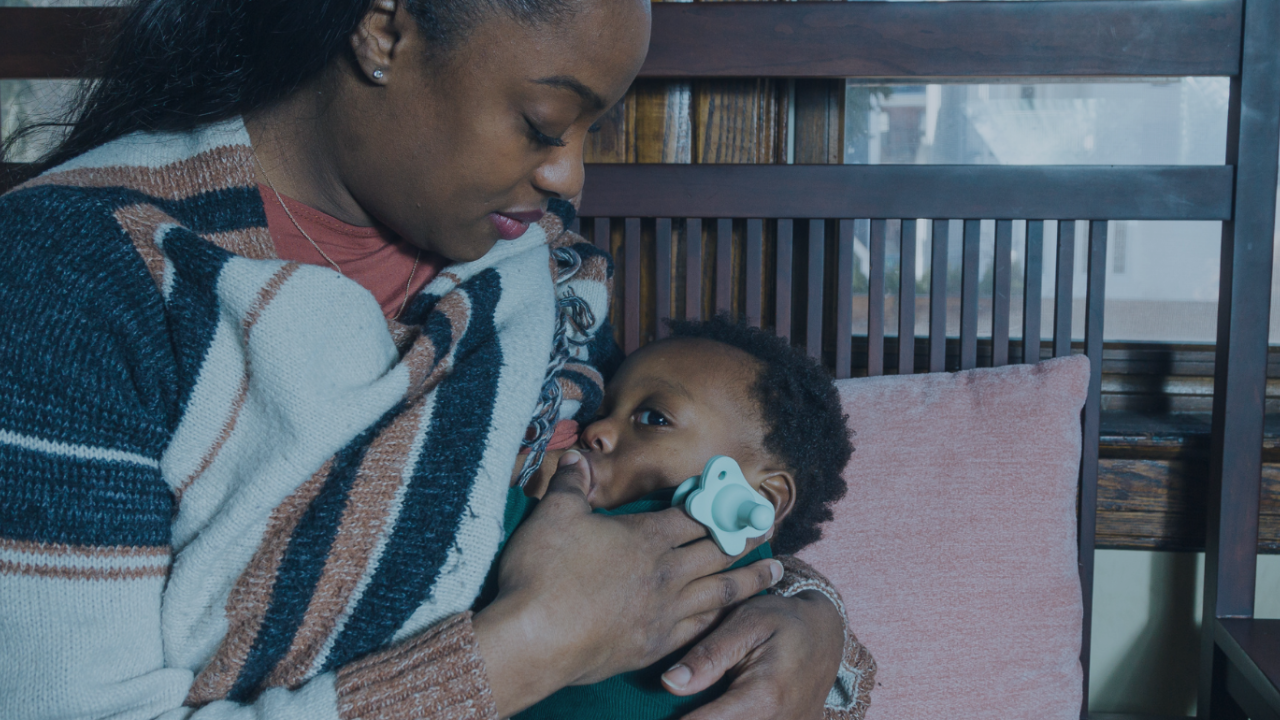 Woman cradling sleeping baby on bench in soft, intimate indoor scene