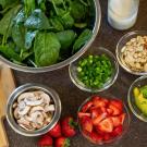 A kitchen counter with an array of ingredients including spinach, strawberries, avocado, almonds, cheese and mushrooms to prepare a salad.